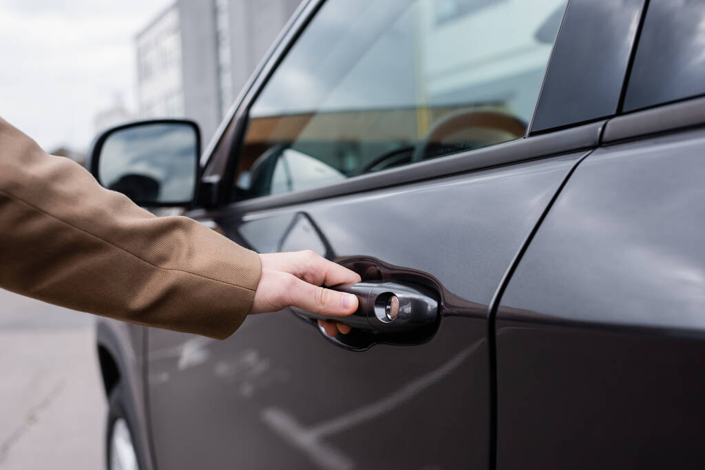 Cropped view of male hand reaching black shiny car door