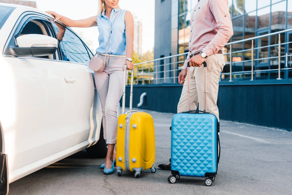 Cropped view of couple standing near car holding luggage
