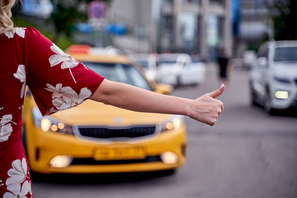outstretched hand stopping taxi in afternoon on blurred background of modern city
