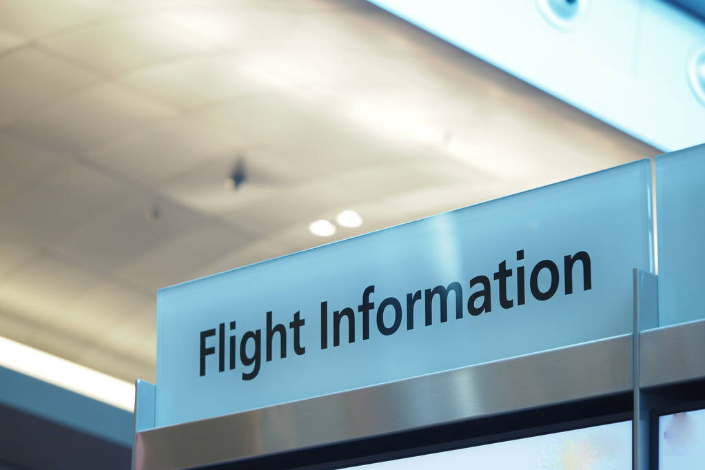 Passengers check flight details at an airport information board.