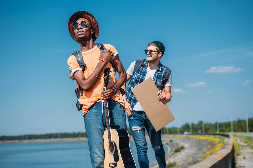 Man with a guitar hitchhiking with friend